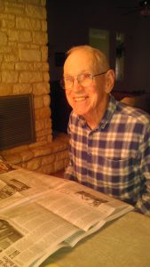 An older man smiling reading a news paper